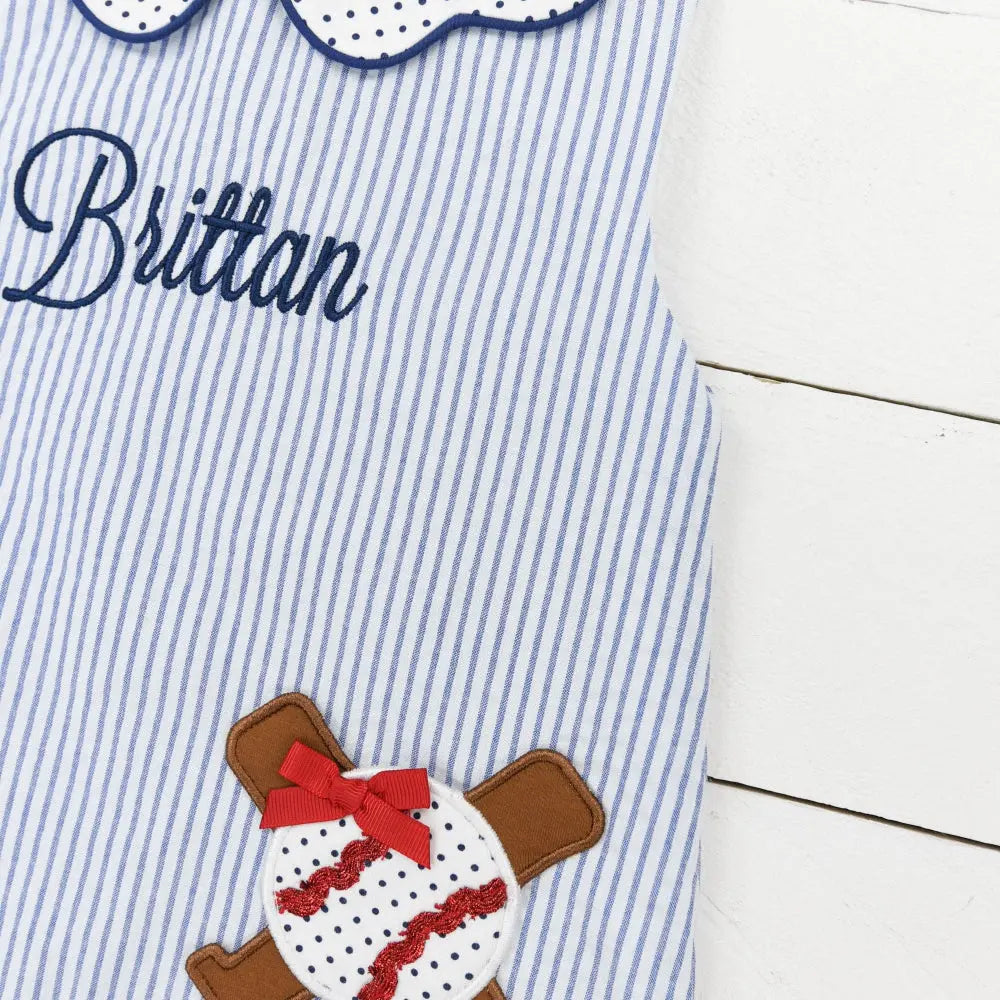 Children's dress with a baseball and bat design and embroidered name on a white wooden background