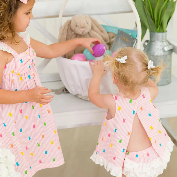 Two young girls in matching pink dresses with colorful polka dots standing in a room.