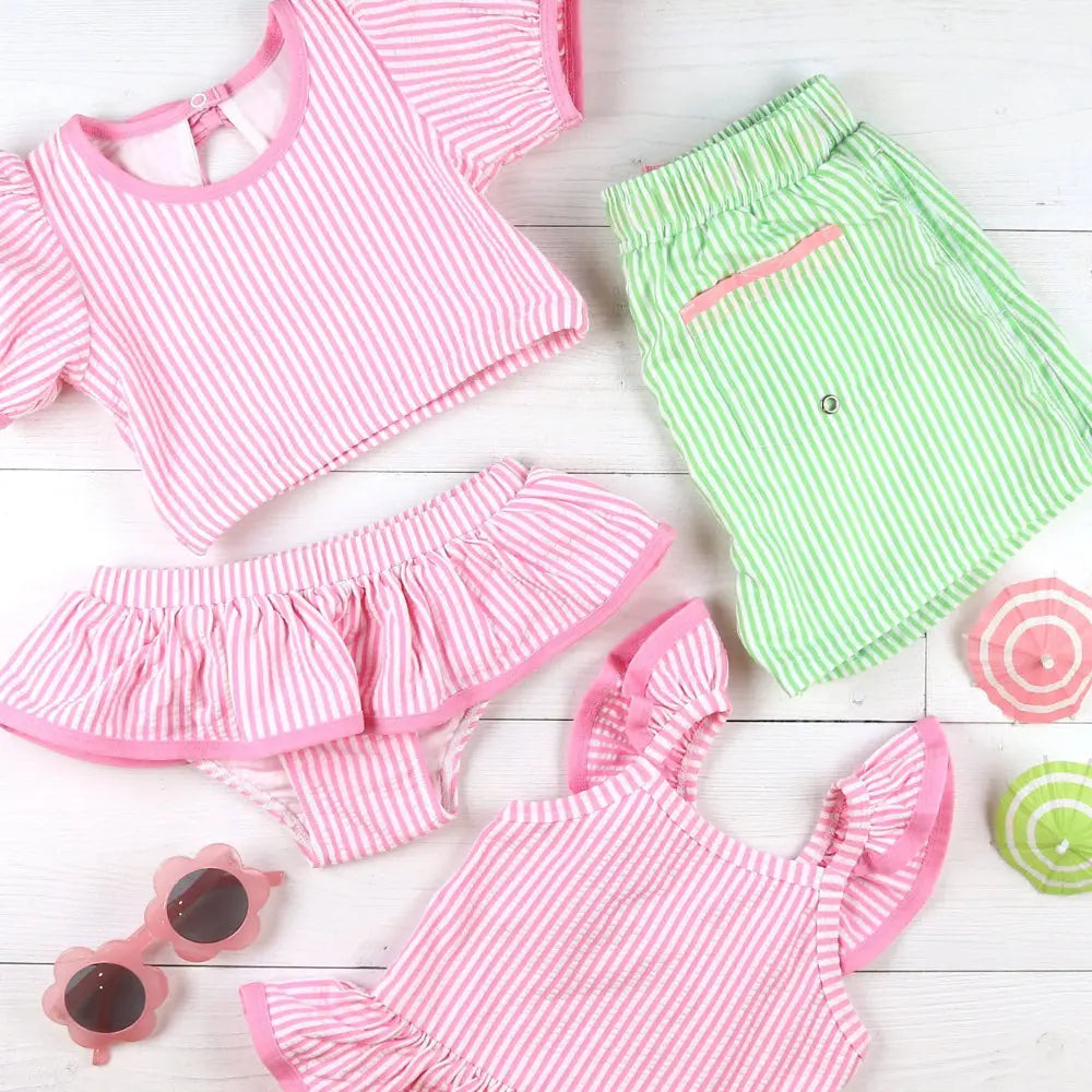 Children's pink and green striped outfit with matching accessories on a light wooden surface.