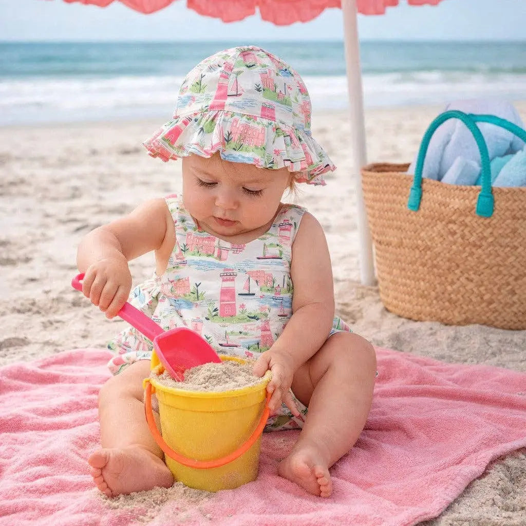 Child playing on a beach with a pink umbrella, towel, and sand toys.
