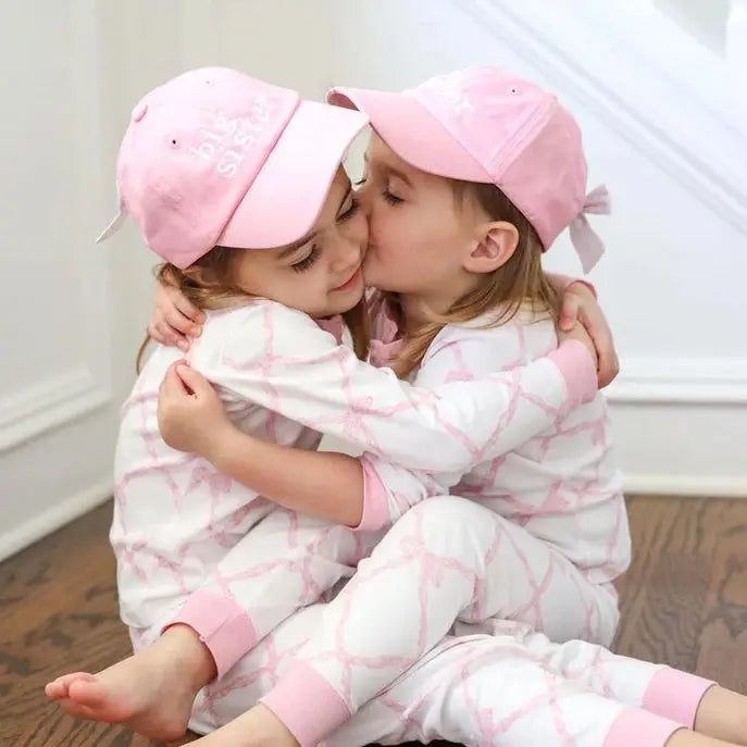 Two children in matching pink and white pajamas hugging on a wooden floor.