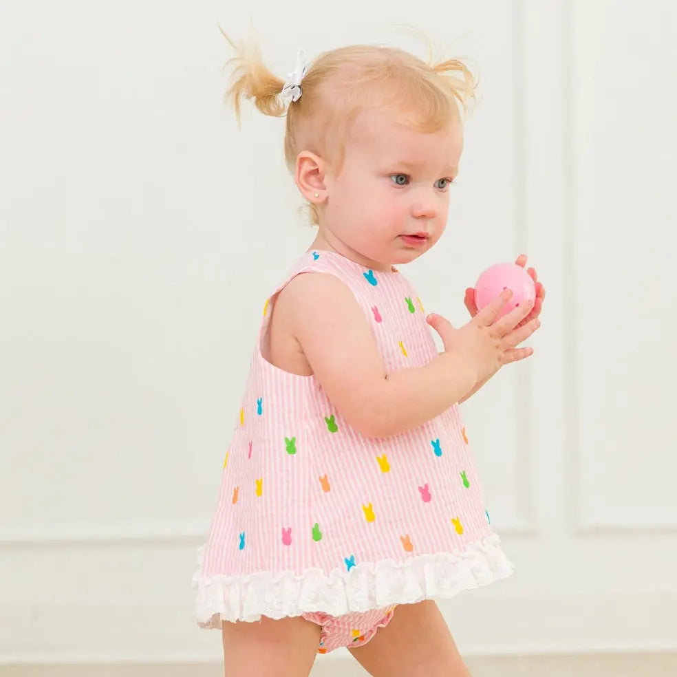 Young girl in a pink dress with colorful details holding a pink toy against a white background