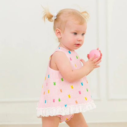 Young girl in a pink dress with colorful details holding a pink toy against a white background