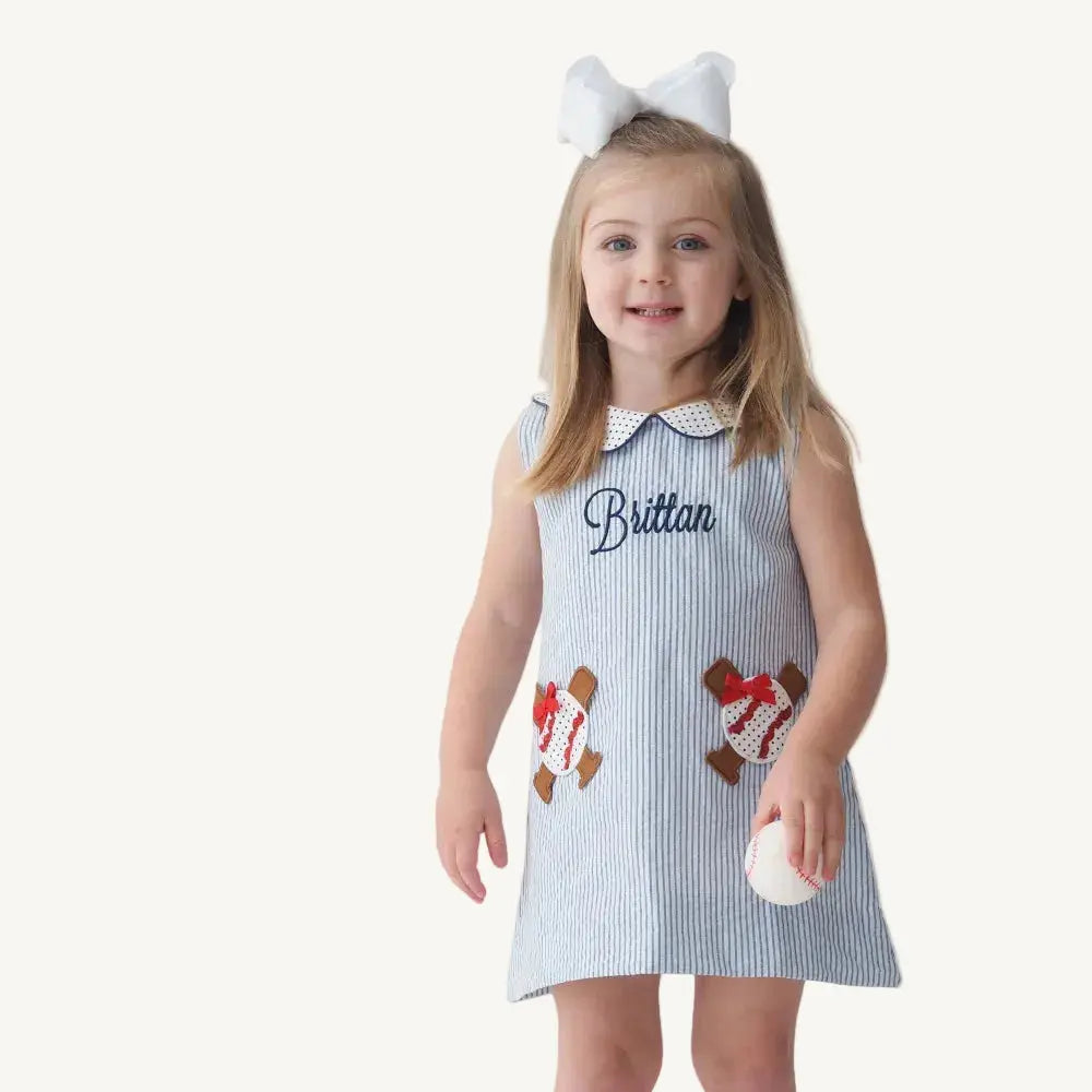 Young girl wearing a dress with gingerbread men and the name 'Brittan' on a plain background