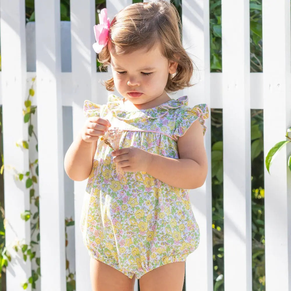 Young girl in a floral dress standing in front of a white lattice background