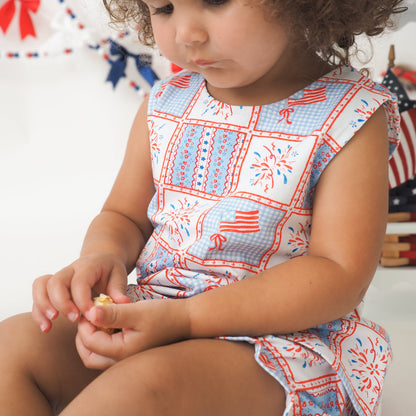 Child wearing a red, white, and blue patterned outfit with American flags.