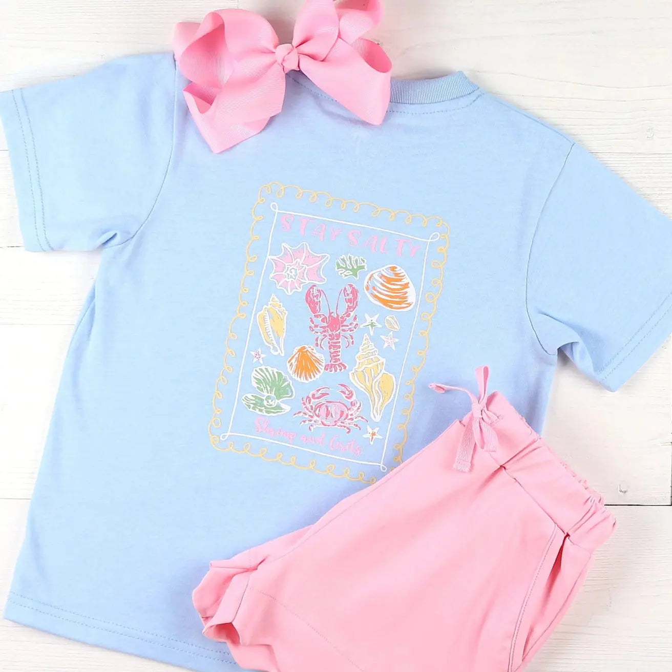 Light blue t-shirt with sea-themed design and pink shorts on a white background