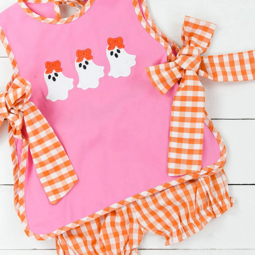 Pink dress with ghost designs and orange checkered details on a white wooden background