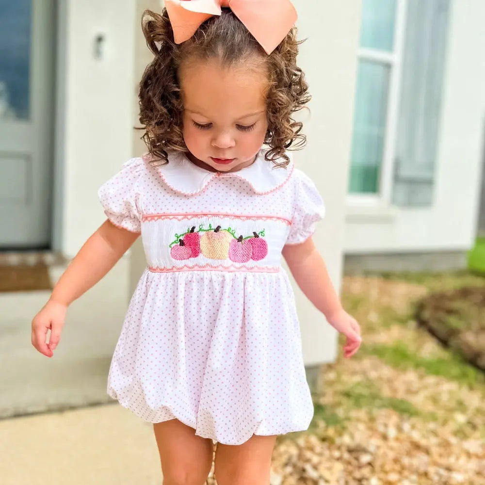 Young girl wearing a white dress with pink accents and a large bow outdoors.