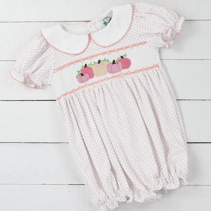 White baby romper with pink accents on a light wooden surface