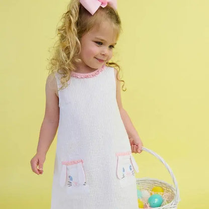 Young girl in a white dress with pink accents holding an Easter basket against a yellow background