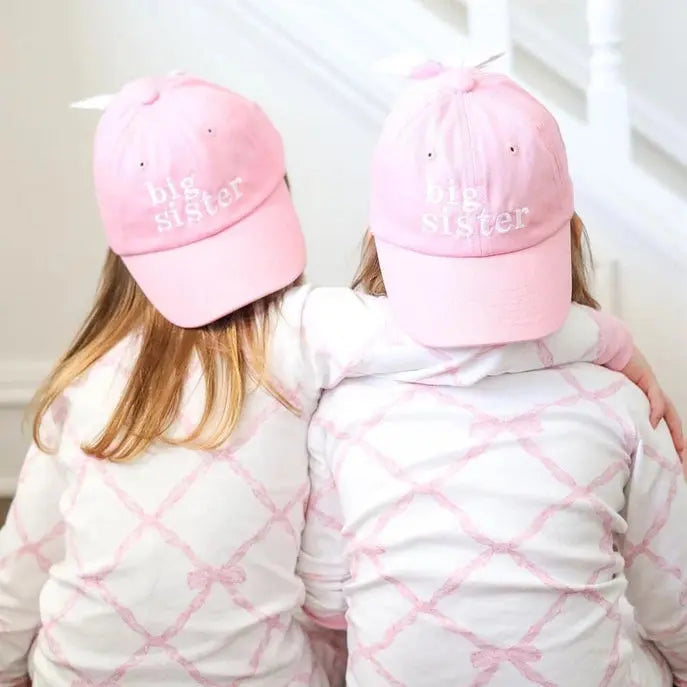 Two children wearing pink 'Big Sister' hats and matching outfits.