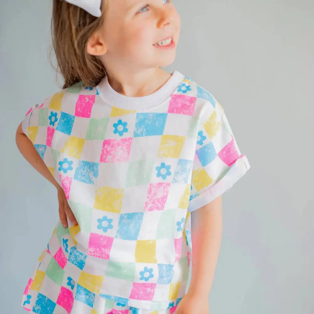 Child wearing a colorful checkered outfit with a white bow on a gray background