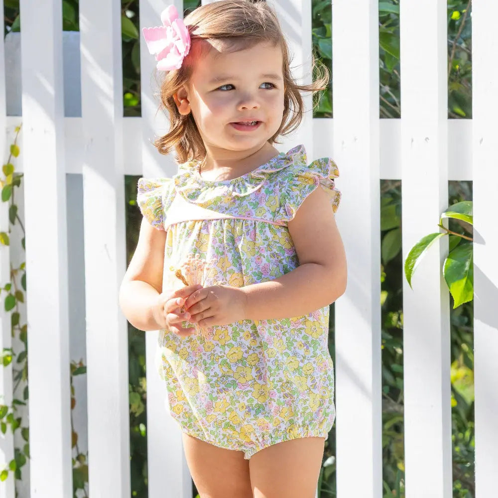 Young girl wearing a floral dress standing in front of a white lattice background