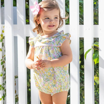 Young girl wearing a floral dress standing in front of a white lattice background
