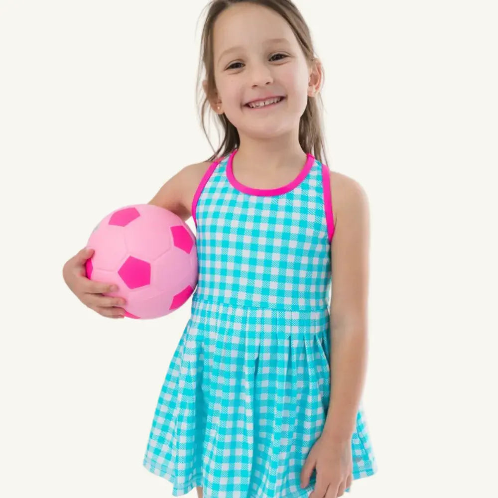 Young girl in a blue checkered dress with pink trim holding a pink soccer ball on a white background